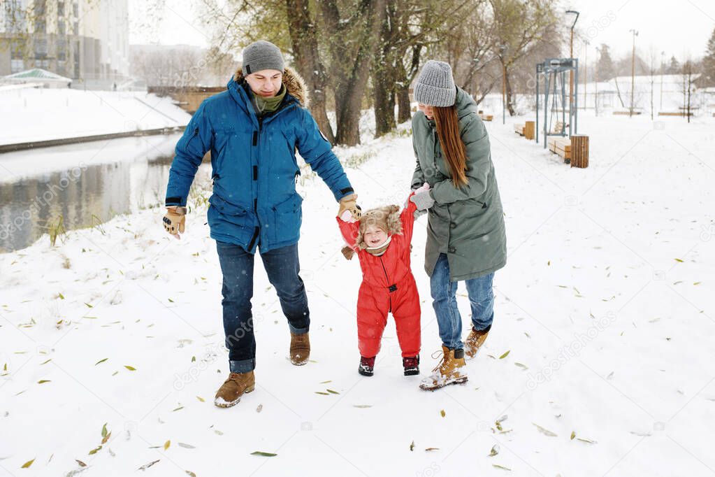 Full height of happy family with one toddler in winter casual outfit walking having fun outdoors in snow public park 