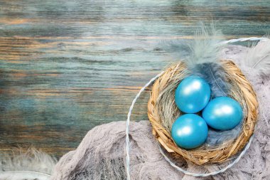 Yuvada renkli yumurtalar, ahşap tepside tüyler, uzay manzaralı mavi paskalya arkaplanı