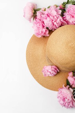 Yaz, bahar konsepti, saman örgülü şapka, beyaz arka planda pembe şakayık çiçekleri, üst manzara.