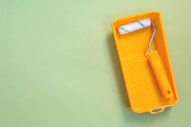 New painting roller in yellow paint tray on pastel green background top view flat lay