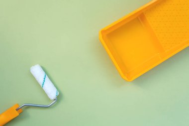 Pastel yeşil zemin üzerinde yeni boya rulosu ve sarı boya tepsisi düz yatıyordu.