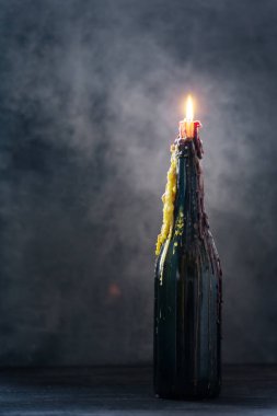 Kavurucu mum ve eritilmiş balmumu koyu arka planda bir şişe, cadılar bayramı süslemesi mistik ışık ile