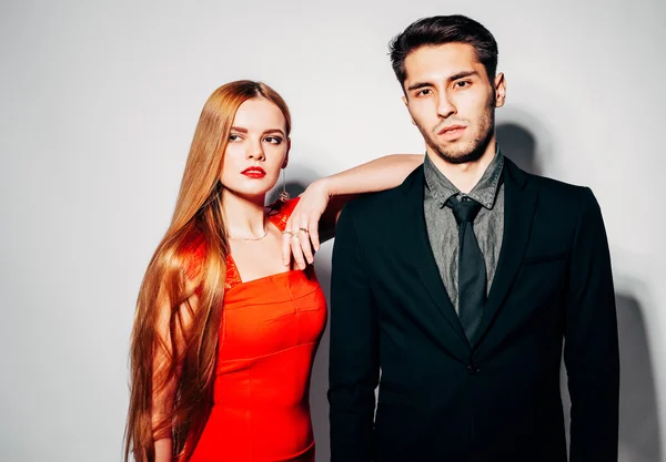 Young fashion man and woman against white wall, posing for the camera. Indoor. Warm color.