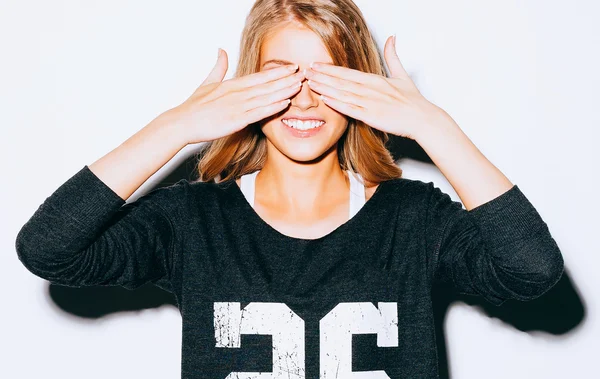 Funny lifestyle portrait beautiful blond crazy girl closes eyes with her hands , in Sweatshirt and white shorts, having fun, emotional and happy mood. Close up. Indoor. Warm color. — Stock Photo, Image