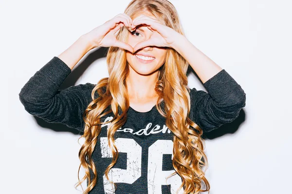 Love. Closeup portrait smiling happy young woman with long blon hair, making heart sign, symbol with hands white wall background. Positive human emotion expression feeling life perception attitude bod