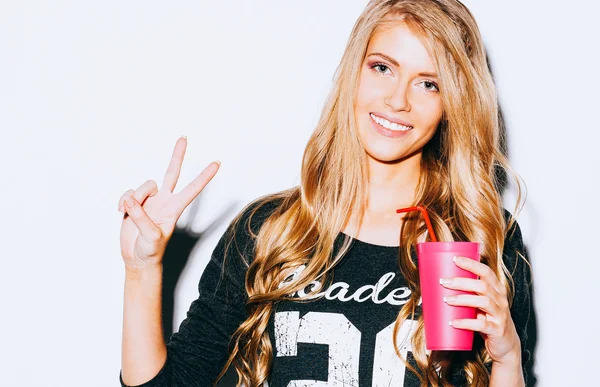 Happy Young Woman Showing Victory Sign and holding a pink glass with straw in hand On White Background. Close up. Indoor. Warm color. — Stock Photo, Image