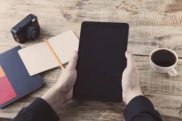 Digitaler Tablet-Computer in männlicher Hand über Café-Hintergrund - Holzplanken, Tasse Kaffee, Nootbook, Bleistift, Vintage-Kamera. Hipster-Stil. Ansicht von oben mit Kopierraum. Freiraum für Text. — Stockfoto