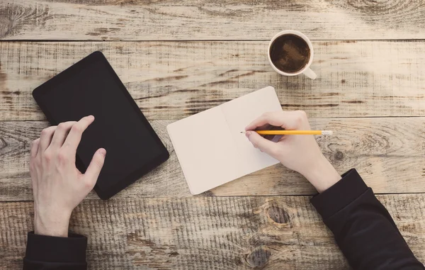 Computador de pastilha digital em mãos masculinas sobre o fundo de café - tábuas de madeira de mesa, xícara de café, caderno, lápis. Estilo Hipster. Vista superior com espaço de cópia. Espaço livre para texto . — Fotografia de Stock