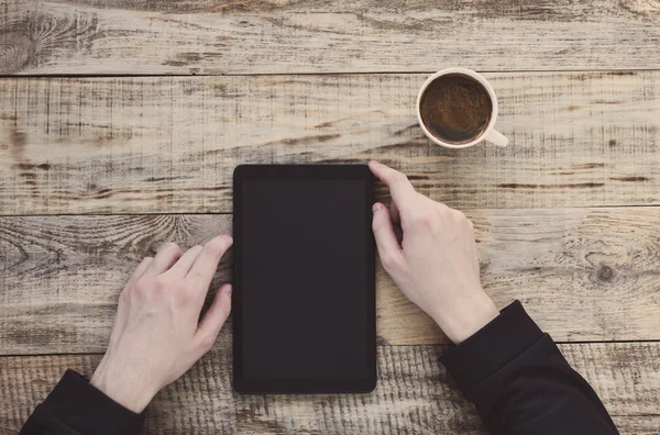 Digital tablet computer in male hands over cafe background - table wooden planks, cup of coffee. Hipster style. Top view with copy space. Free space for text. — Stock Photo, Image