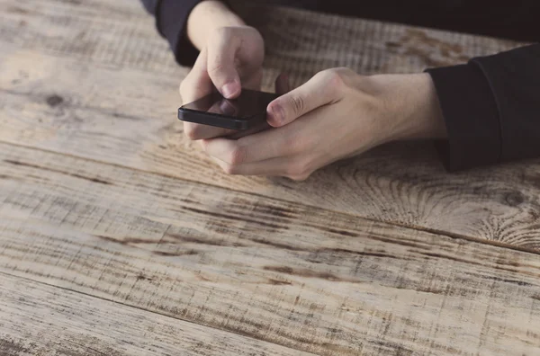 Großaufnahme männlicher Hände, die ihr Smartphone in der Hand halten und mit dem Finger auf Grafik und Text auf dem Bildschirm an Holzplanken am Tisch zeigen. Hipster-Stil. Freiraum für Text. — Stockfoto