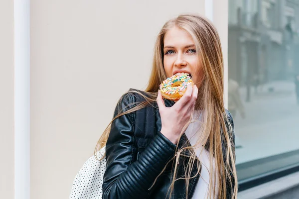 Attractive young blond sexy woman eating tasty colorful donut. Outdoors lifestyle portrait of pretty girl — Stock Photo, Image