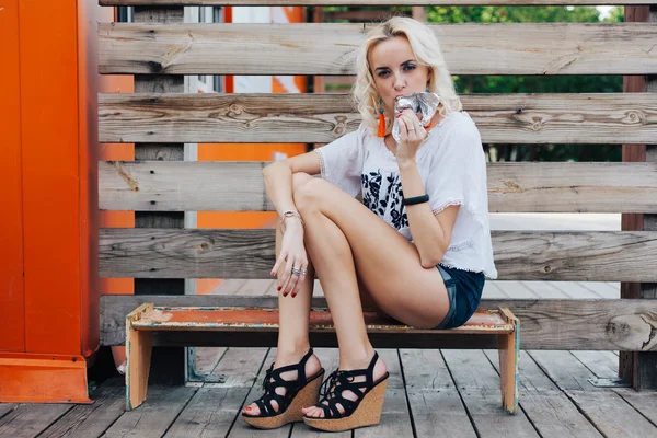 Junge schöne Frau mit langen Beinen in high Heels auf Brettern sitzen und Essen ein Eis an einem lauen Sommerabend. Außen. — Stockfoto