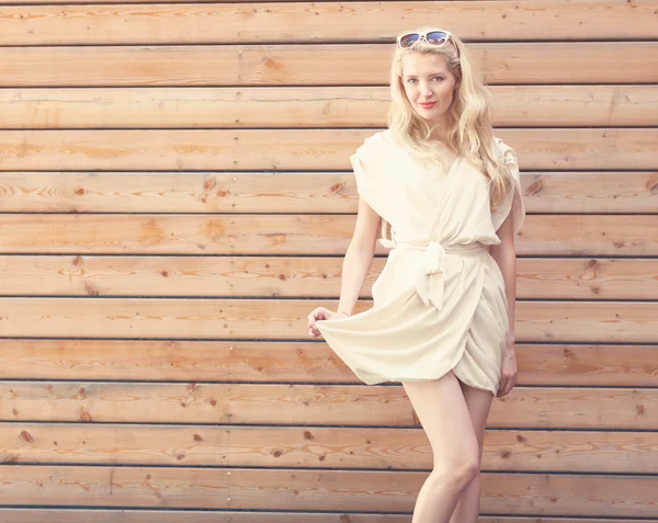 Buiten zomer sensuele mode portret mooie jonge blonde vrouw liften de rand van een witte jurk permanent op de achtergrond van houten planken. afgezwakt in warme kleuren — Stockfoto