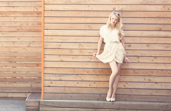 Buiten zomer sensuele mode portret mooie jonge blonde vrouw liften de rand van een witte jurk permanent op de achtergrond van houten planken. afgezwakt in warme kleuren — Stockfoto