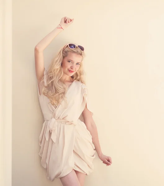 Summer portrait of young beautiful blond woman in white dress posing near the wall and have fun. Toned in warm colors — Stock Photo, Image