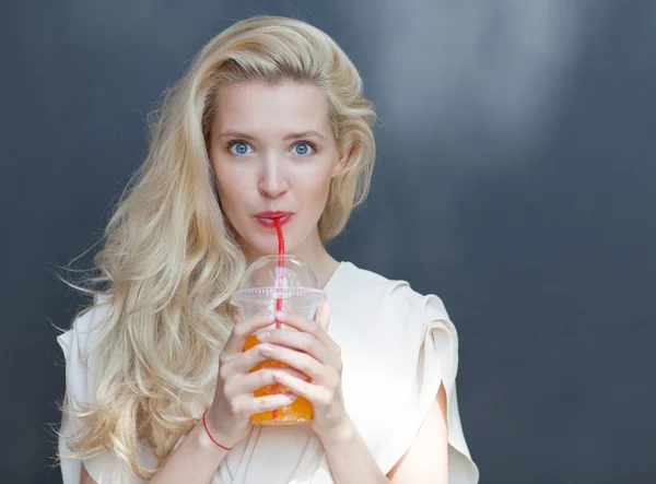 Beautiful sexy blonde with blue eyes drinking beverage through a straw on a hot summer day near the wall — Stock Photo, Image