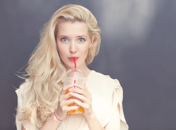 Beautiful sexy blonde with blue eyes drinking beverage through a straw on a hot summer day near the wall. Toned in warm colors — Stock Photo, Image