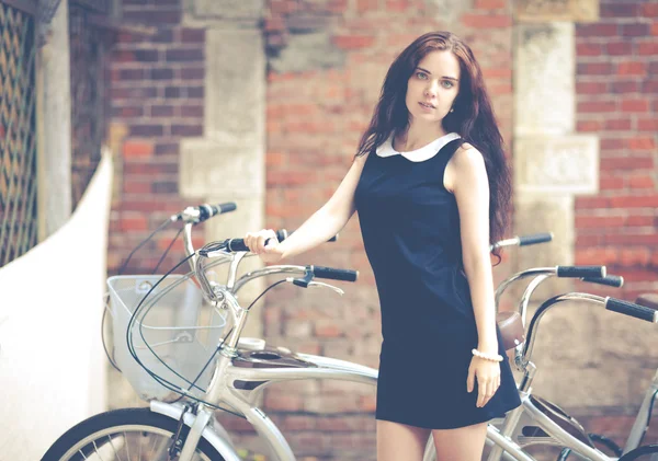 Bella bruna con i capelli lunghi in piedi vicino a una bicicletta. Foto hipster colorato — Foto Stock