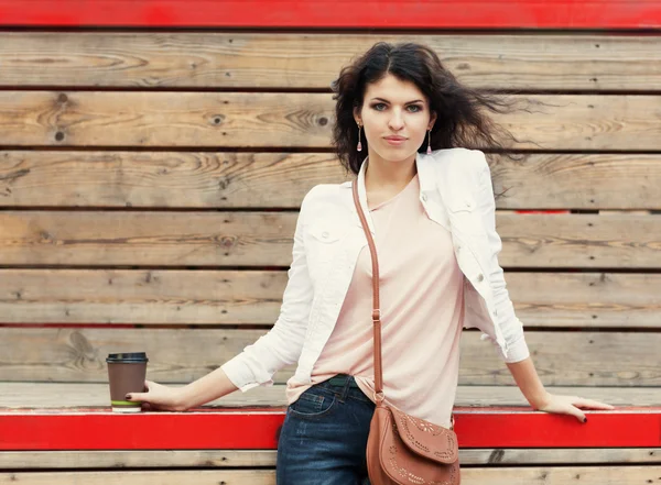 Hermosa chica alta con el pelo largo morena en jeans de pie sobre tablones de madera viejos con una taza de café en la mano en una cálida noche de verano —  Fotos de Stock