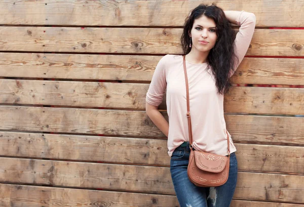 Beautiful brunette girl stands near a wall wooden planks — Stock Photo, Image