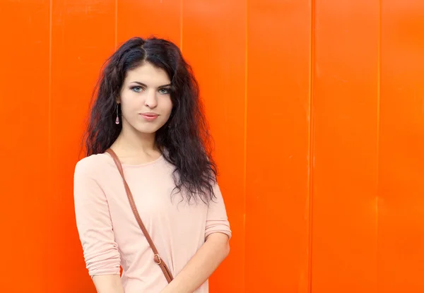 Высокая девушка с длинными волосами брюнетка, стоящая на фоне оранжевой стены — стоковое фото