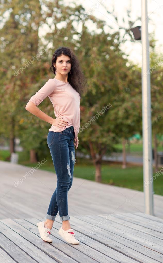 Beautiful tall girl with long hair brunette in jeans standing on old wooden  planks on a warm summer evening Stock Photo by ©Superlime 53017169