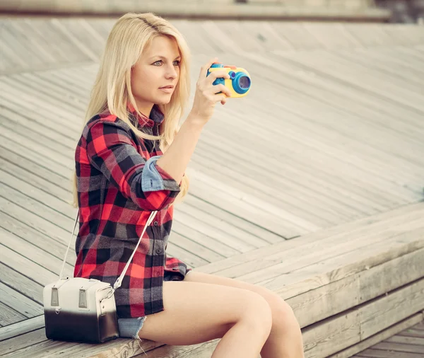 Attraente donna bionda seduta sul pavimento di legno e fotografata con una macchina fotografica giocattolo — Foto Stock