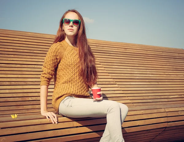 Hermosa joven sentada en un banco en un cálido día de verano whis cuo de café — Foto de Stock