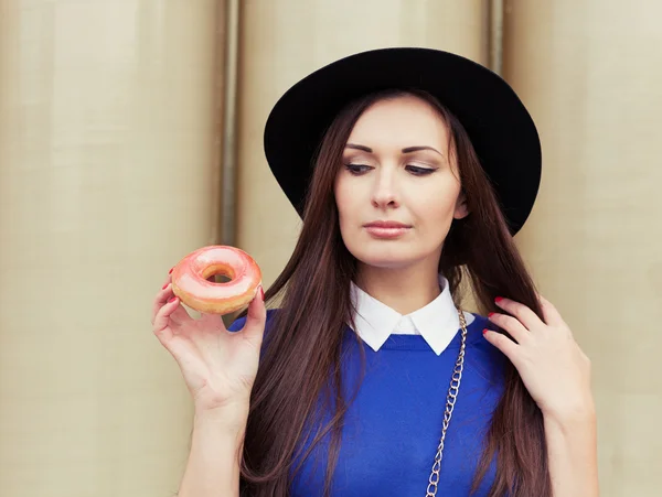 Hermosa chica morena en busca de un sabroso donut rosa — Foto de Stock