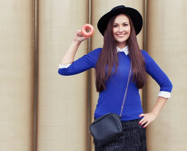 Beautiful brunette girl shows a tasty pink donut — Stock Photo, Image