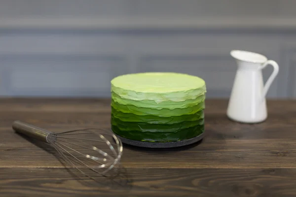 Beautiful green cake stands on dark wooden board, close corolla and white pitcher — Stock Photo, Image