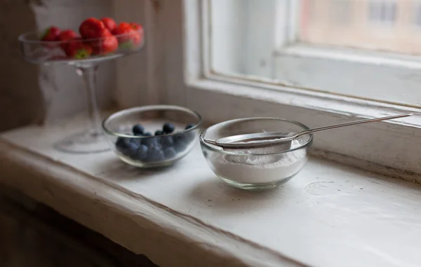 Blueberries strawberries icing sugar in a small bowl at the window — Stock Photo, Image