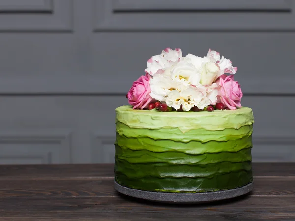 Vacker grön tårta dekorerad med blommor står på mörk träskiva — Stockfoto