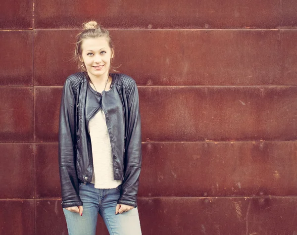 Menina em uma jaqueta de couro preto posando em uma parede de metal enferrujado. Ao ar livre — Fotografia de Stock