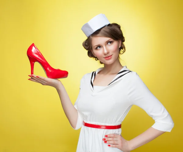 Bella pin-up ragazza vestita da marinaio mantiene le scarpe rosso palmo. sfondo giallo, primo piano — Foto Stock