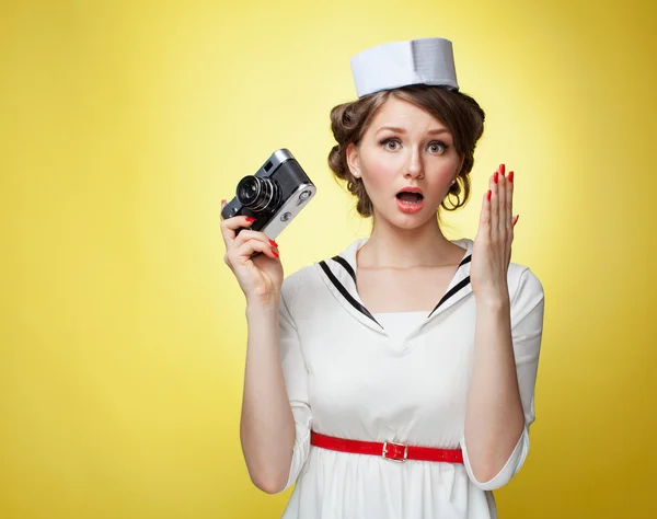 Gyönyörű pin-up lány öltözött egy tengerész egy vintage kamera és sikolyok mögött a kezét. Sárga háttér, közelről — Stock Fotó