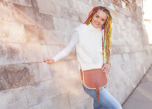 Renkli dreadlocks ile güzel kız beyaz bir ceket duvara yakın poz onun omuz eğlenceli üzerinde vintage kahverengi çantalı yaz güneşli bir günde — Stok fotoğraf