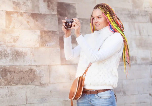 Piękna dziewczyna z kolorowych dredy letni, słoneczny dzień w białą kurtkę z rocznika brązową torebkę na jej ramieniu starodawny aparat ma zdjęcie — Zdjęcie stockowe