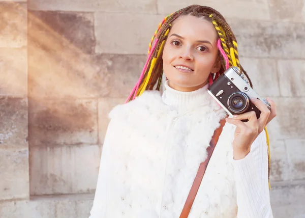 Beautiful girl with colored dreadlocks summer sunny day in a white jacket with a vintage brown bag over her shoulder holding in her hand vintage camera — Stock Photo, Image