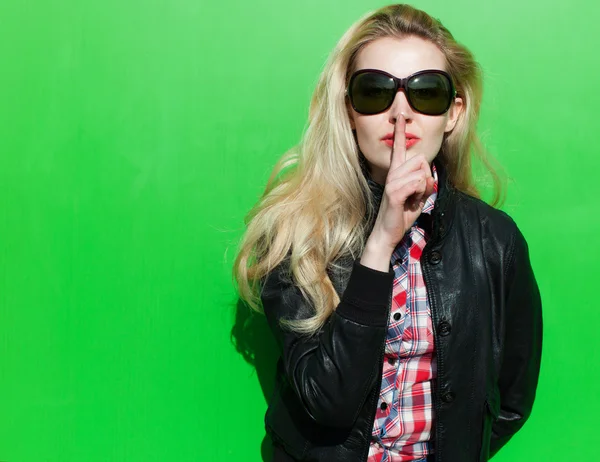Prachtige blond meisje zonnige zomerdag in de zwarte jas en lippen vinger vragen om stilte — Stockfoto