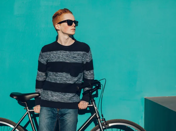 Jeune rouquine homme debout à côté d'un vélo vintage dans des lunettes près du mur turquoise chaude journée ensoleillée d'été — Photo