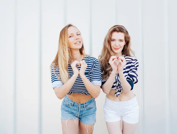 Porträt zweier wunderschöner modischer Freundinnen in Jeanshosen und gestreiften T-Shirts, die Herzform mit Händen zeigen. Draußen. positive Emotionen haben, schreien und lachen, heller Sommertag. — Stockfoto