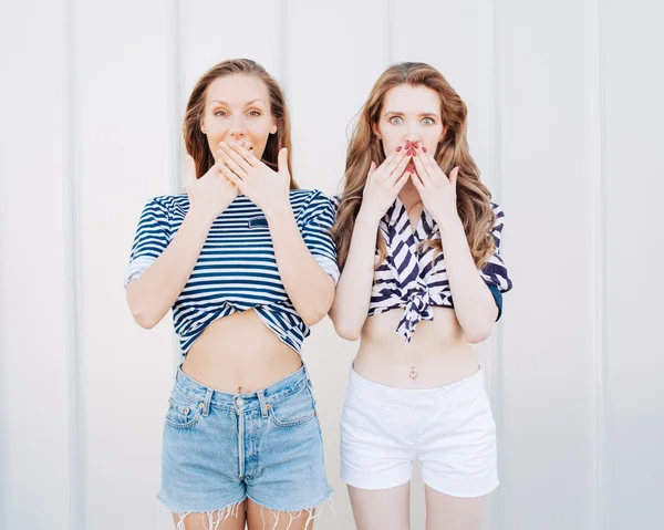 Porträt von zwei schönen modischen Freundinnen in Jeanshosen und gestreiftem T-Shirt, die neben der Glaswand posieren. positive überraschende Emotionen haben, schreien und lachen, heller Sommertag. — Stockfoto