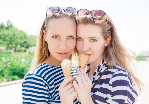 Junge sexy blonde beste Freundinnen, die bei sommerlich heißem Wetter mit Sonnenbrille Eis essen, haben Spaß und gute Laune, schauen in die Kamera und lächeln. warme Farben. Außenbereich — Stockfoto