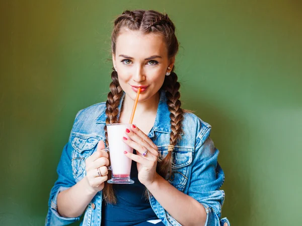 Hermosa chica con trenzas sentada en un café y bebiendo un batido, relajándose ante la cámara — Foto de Stock