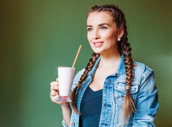 Красива дівчина з косами, сидячи в кафе і п'ючи молочний коктейль, дивиться у вікно — стокове фото