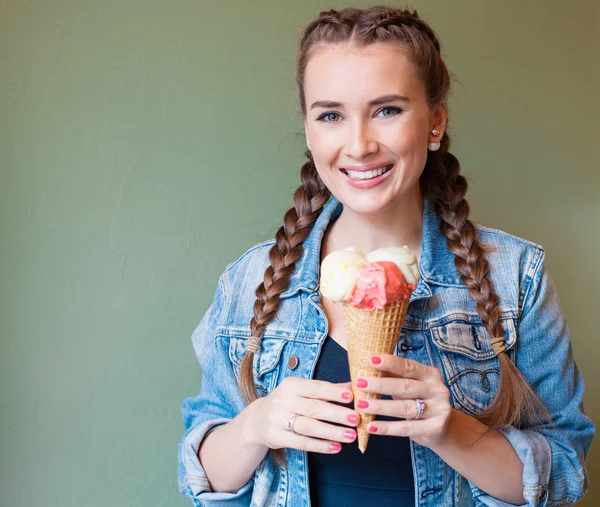 Beautiful girl with braids sitting in a cafe. She holds a huge multi-colored ice cream in waffle cone — Stock Fotó