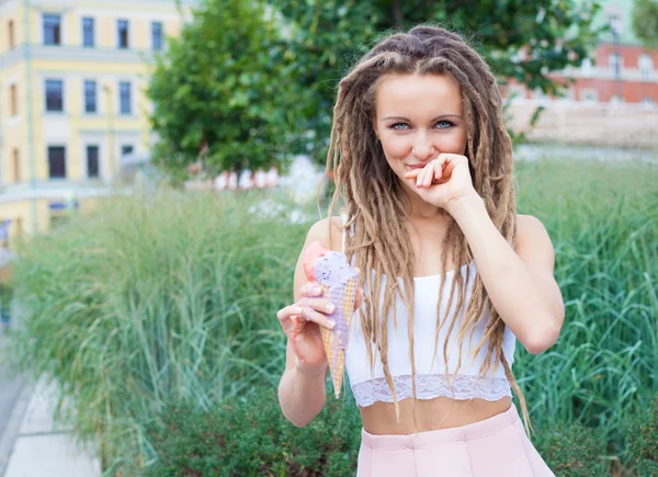 Menina loira sexy nova com dreads comer sorvete multicolorido em cones waffle na noite de verão, alegre e alegre. Centro da cidade europeia, no parque. Olha para a câmara. — Fotografia de Stock