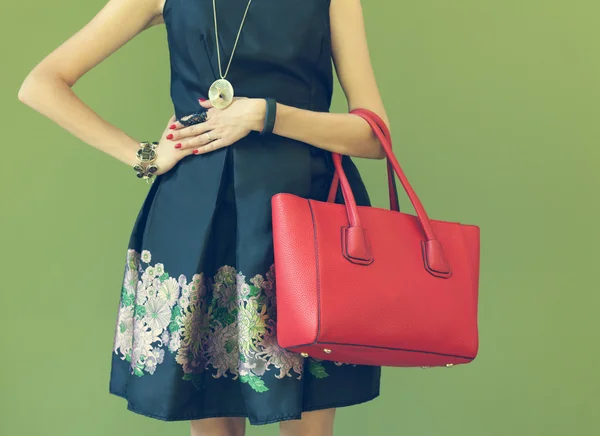 Bolsa vermelha bonita na moda no braço da menina em um vestido preto na moda, posando perto da parede em uma noite quente de verão. Cor quente — Fotografia de Stock