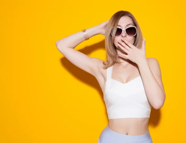 Beautiful fashionable girl posing in a skirt and top with sunglasses on a yellow background covering her mouth with his hand. Gorgeous Woman Portrait. Stylish Haircut and Makeup. Hairstyle. Make up. S — Stock Photo, Image